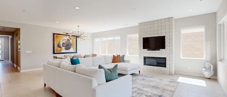A modern living room with a white sofa, a fireplace, and a large TV.