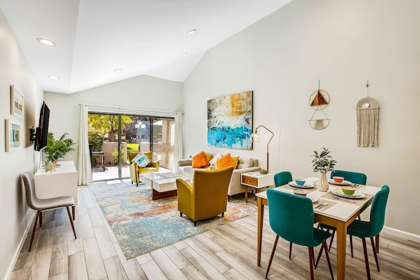 A modern living room with a dining area, featuring a sofa, chairs, a coffee table, and a rug. - Beautifully updated mid-century condo with shared pool/spa & mountain views (Palm Springs)