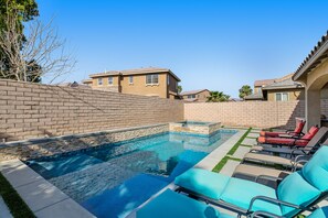 A swimming pool with lounge chairs, a brick wall, and a clear blue sky. - Inviting and unique dog-friendly home with pool, pool spa, firepit, & W/D (Indio)