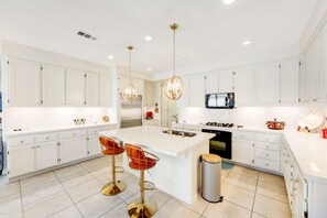 A modern kitchen with white cabinetry, a large island with stools, stainless steel appliances, and pendant lighting. - Inviting and unique dog-friendly home with pool, pool spa, firepit, & W/D (Indio)