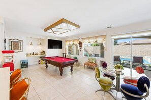 Ein geräumiger Raum mit Poolbillard, bequemen Sitzgelegenheiten und großen Fenstern mit Blick ins Freie.