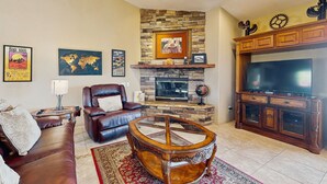 A living room with a stone fireplace, leather sofa, and a large flat-screen TV. - Luxurious Dog-Friendly home with an outdoor kitchen, private pool, spa, & casita (Bermuda Dunes)