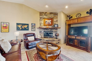 A living room with a stone fireplace, leather sofa, and a large flat-screen TV. - Luxurious Dog-Friendly home with an outdoor kitchen, private pool, spa, & casita (Bermuda Dunes)