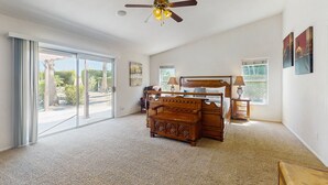 A spacious bedroom with a large sliding glass door leading to a balcony, a wooden bed, a nightstand, and a ceiling fan. - Luxurious Dog-Friendly home with an outdoor kitchen, private pool, spa, & casita (Bermuda Dunes)