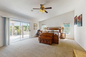 A spacious bedroom with a large sliding glass door leading to a balcony, a wooden bed, a nightstand, and a ceiling fan. - Luxurious Dog-Friendly home with an outdoor kitchen, private pool, spa, & casita (Bermuda Dunes)
