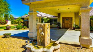 A building with a covered entrance, a stone fountain, and a well-maintained garden. - Luxurious Dog-Friendly home with an outdoor kitchen, private pool, spa, & casita (Bermuda Dunes)