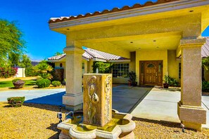 A building with a covered entrance, a stone fountain, and a well-maintained garden. - Luxurious Dog-Friendly home with an outdoor kitchen, private pool, spa, & casita (Bermuda Dunes)
