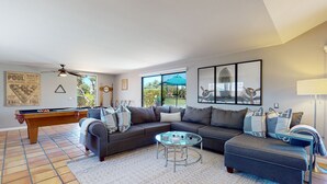 Ein Wohnzimmer mit Billardtisch, einer Couch, einem Couchtisch und Blick ins Freie.