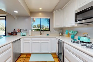 A modern kitchen with white cabinets, a stainless steel range hood, a window with a view, and a teal kettle on the counter. - Lovely midcentury home with private pool and outdoor kitchen - dogs welcome (Bermuda Dunes)