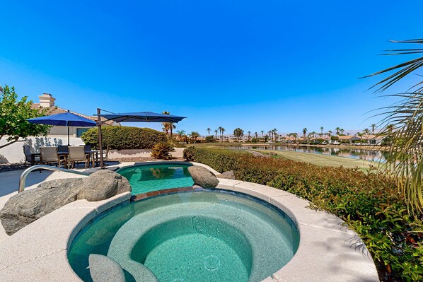 Une piscine avec un jacuzzi, entourée d’un jardin aménagé et offrant une vue sur un lac.