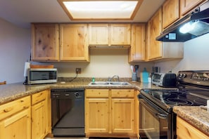 A kitchen with wooden cabinets, a microwave, a dishwasher, a sink, a toaster, and a stove. - Condo with full kitchen, balconies, views of Mt. Elden - close to town (Flagstaff)