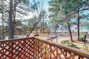 A view from a balcony with a wooden lattice railing, overlooking a parking area with a red car, surrounded by trees and a clear sky. - Condo with full kitchen, balconies, views of Mt. Elden - close to town (Flagstaff)
