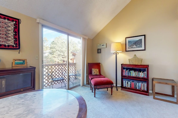 Une pièce avec une table en verre, un fauteuil rembourré de couleur rouge, une bibliothèque et une vue sur l’extérieur, accessible par une porte coulissante.