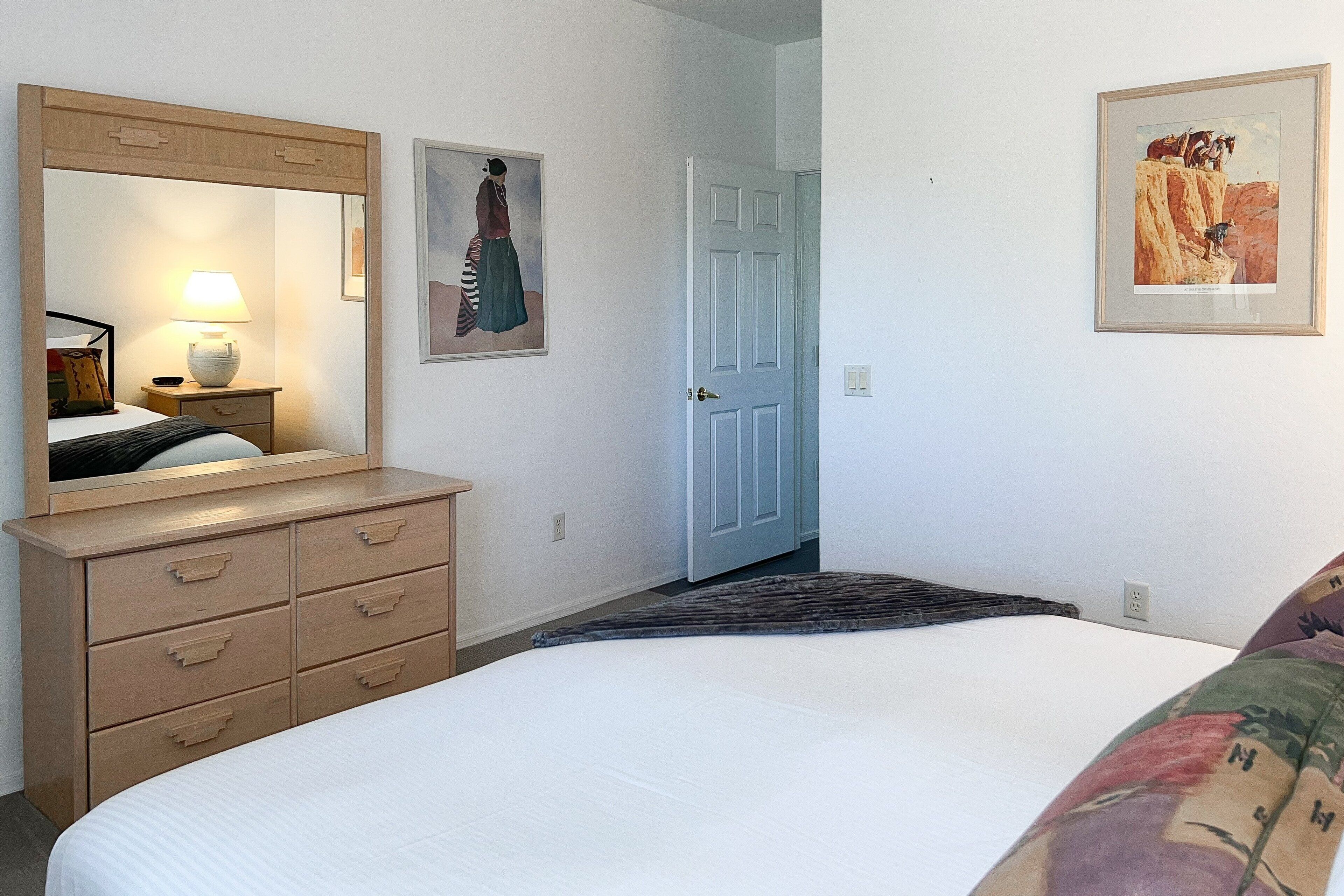 Une chambre à coucher avec un lit, une commode, un miroir et deux tableaux encadrés accrochés au mur.