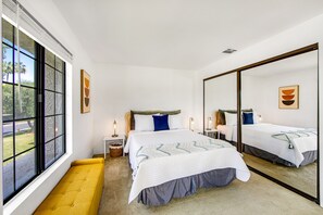 A modern bedroom with a large bed, a bench, a large window, and a mirror. - Second floor, dog-friendly condo w/ pool & hot tub access, WiFi, and central AC (Palm Springs)