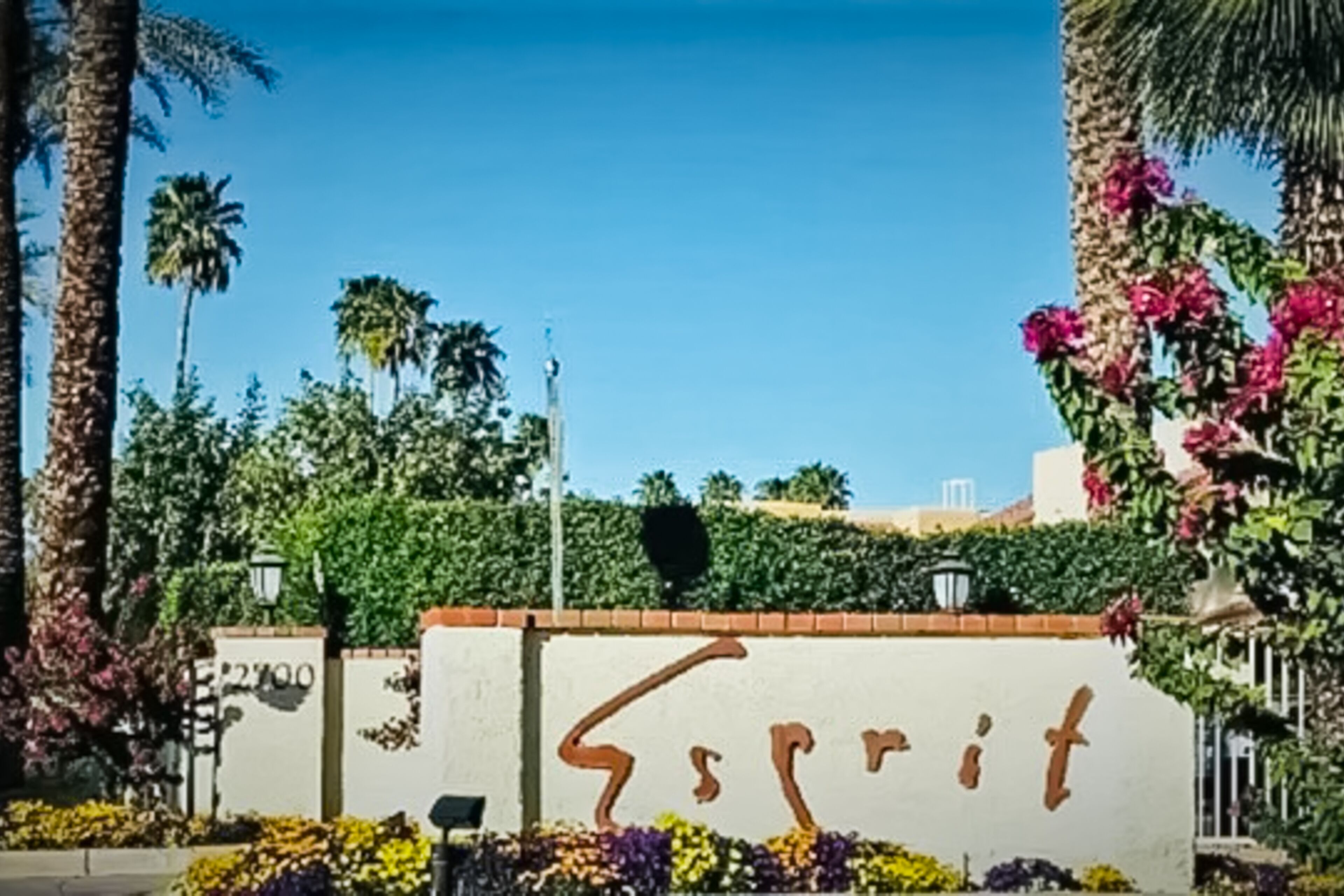 Ein Gebäudeeingang mit einem Schild, das "Esprit" zeigt, umgeben von Palmen und blühenden Pflanzen.