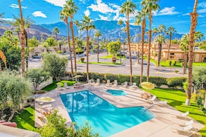 A pool area with lounge chairs and umbrellas, surrounded by palm trees and a view of mountains. - Dog-friendly, ground-floor, mountain view condo with 2 patios, pool & hot tub (Palm Springs)