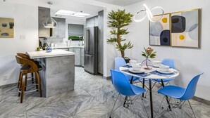 Een moderne keuken met een centraal eiland, barstoelen en een eethoek met blauwe stoelen en een tafel voor vier personen.