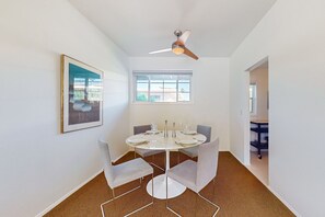 Ein Essbereich mit einem runden Tisch, sechs Stühlen, einem Deckenventilator, einem Fenster und einem gerahmten Bild an der Wand.