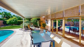 Un patio exterior con piscina, un área de comedor cubierta y vistas a una piscina.