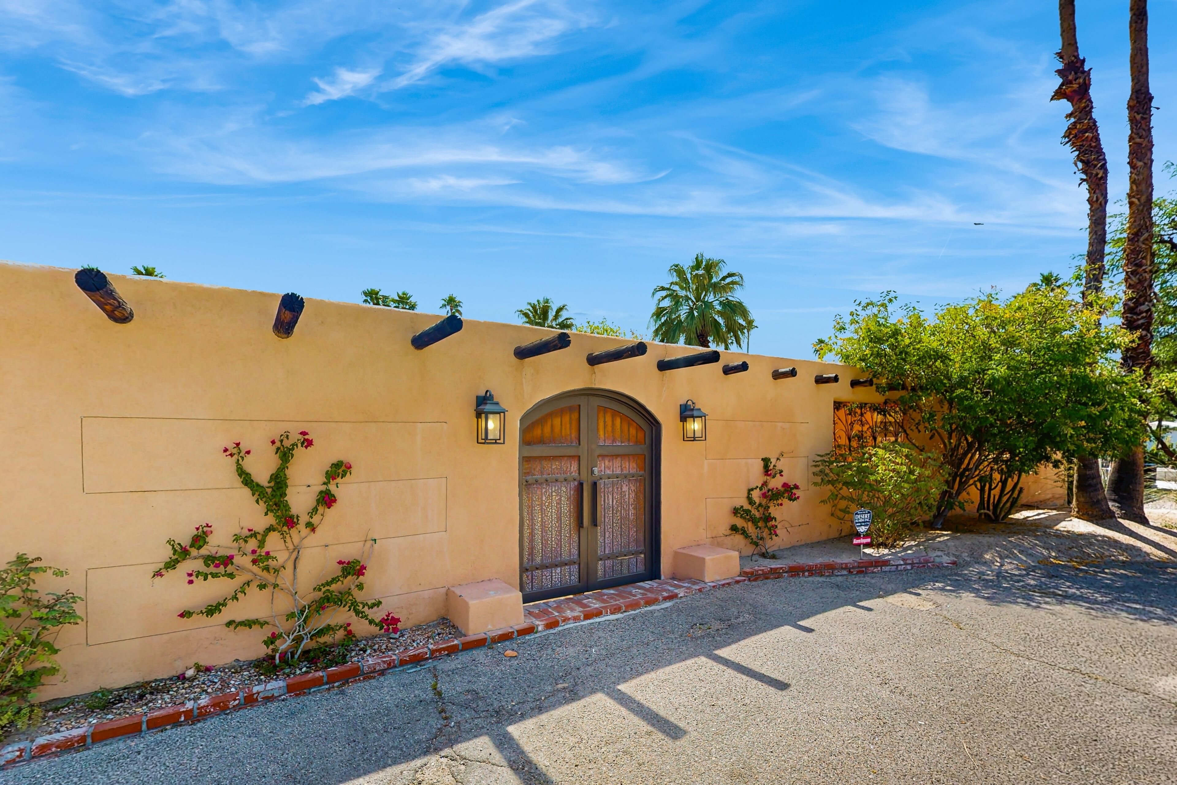 A building with a stucco exterior, a wooden door with glass panels, and a brick pathway leading to the entrance.