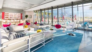 A modern lounge area with seating, a bar, and large windows offering a view. - Chic dog-friendly home with private pool, pool spa, gym, pools, grills & firepit (Palm Springs)