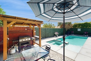 A backyard with a barbecue grill, a table with chairs, a pool, and a pergola with an umbrella. - Adorable adobe-style oasis with private pool & pool spa - dog-friendly (Palm Springs)