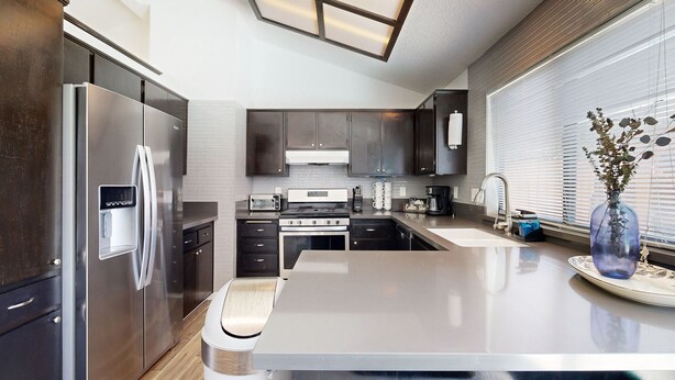 Una cocina moderna con una isla central, electrodomésticos de acero inoxidable y un ventanal con persianas.