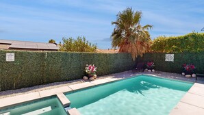 Una piscina con seto, palmera y plantas en macetas.