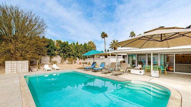 Ein Swimmingpool mit Liegestühlen und Sonnenschirmen, umgeben von einer Terrassenanlage und Palmen.