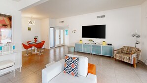 Ein modernes Wohnzimmer mit einem weißen Sofa, einem karierten Sofa, einem Essbereich mit roten Stühlen und einem an der Wand montierten Fernseher.