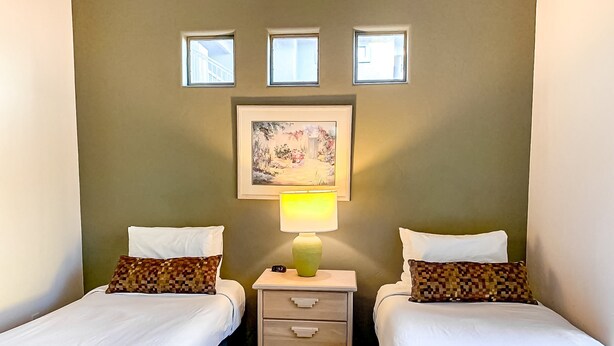 A room with two beds, a nightstand with a lamp, and a framed picture on the wall. - Bright & modern resort condo with pool & hot tub (Oro Valley)