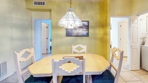 A dining area with a table and chairs, a hanging light fixture, and a door leading to another room. - Bright & modern resort condo with pool & hot tub (Oro Valley)