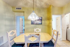 A dining area with a table and chairs, a hanging light fixture, and a door leading to another room. - Bright & modern resort condo with pool & hot tub (Oro Valley)