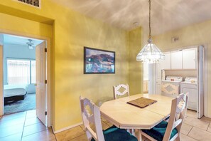 A dining area with a table and chairs, a hanging light fixture, a framed picture on the wall, and a kitchen area with appliances. - Bright & modern resort condo with pool & hot tub (Oro Valley)