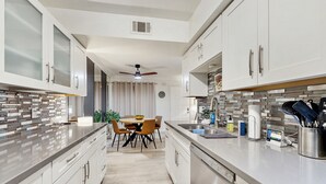 Una cocina moderna con armarios blancos, una zona de comedor con mesa y sillas, y un horno empotrado.