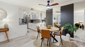 Una cocina moderna con armarios blancos, una isla central y un comedor con mesa redonda y sillas.