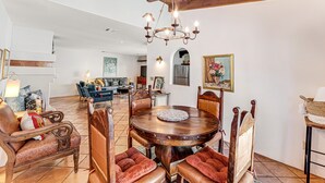 Een eethoek met een houten tafel en stoelen, een kroonluchter, en een woonkamer op de achtergrond.