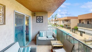 A balcony with a sofa, table, and chairs, overlooking a pool and other buildings. - Dog-friendly condo w/ balcony & shared pools/hot tubs - close to downtown (Palm Springs)