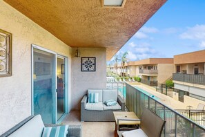 Ein Balkon mit einer Couch, einem Tisch und Stühlen mit Blick auf einen Pool und weitere Gebäude.