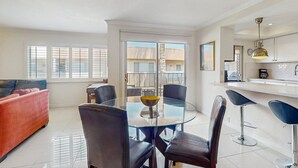 A modern living room with a glass dining table, black chairs, a red sofa, and a kitchen area with a white countertop and bar stools. - Dog-friendly condo w/ balcony & shared pools/hot tubs - close to downtown (Palm Springs)