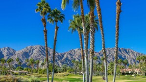 Un parcours de golf bordé de palmiers, avec des montagnes en arrière-plan.
