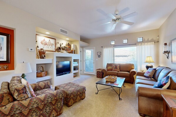 A living room with a sofa set, a television, a ceiling fan, and a fireplace. - Stylish condo with pool, hot tub & lovely mountain views (Oro Valley)