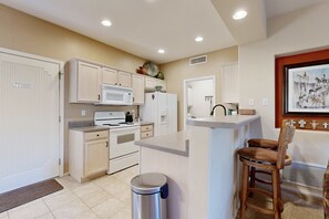 A compact kitchen with white cabinets, a microwave, a refrigerator, and a sink. There is a trash can and a wooden chair. - Stylish condo with pool, hot tub & lovely mountain views (Oro Valley)