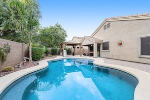 A swimming pool with a curved edge, surrounded by a landscaped garden with various plants and a patio area with outdoor furniture. - Dreamy home with private pool, high-speed WiFi, full kitchen, & W/D (Sun City)