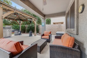 Ein Terrassenbereich im Freien mit Korbmöbeln, einem Grill und einer überdachten Sitzgelegenheit.