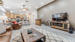 A modern living room with a sofa, coffee table, TV, and kitchen in the background. - Dreamy home with private pool, high-speed WiFi, full kitchen, & W/D (Sun City)