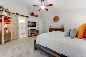 A bedroom with a bed, a television, a ceiling fan, and a clock on the wall. - Dreamy home with private pool, high-speed WiFi, full kitchen, & W/D (Sun City)