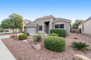 A residential house with a well-maintained front yard, including various shrubs and a gravel driveway. - Dreamy home with private pool, high-speed WiFi, full kitchen, & W/D (Sun City)