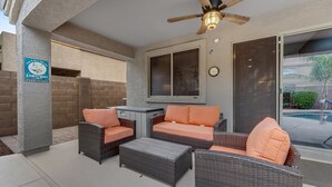 A covered outdoor seating area with wicker furniture and orange cushions, a ceiling fan, and a sign indicating ladies' night. - Dreamy home with private pool, high-speed WiFi, full kitchen, & W/D (Sun City)